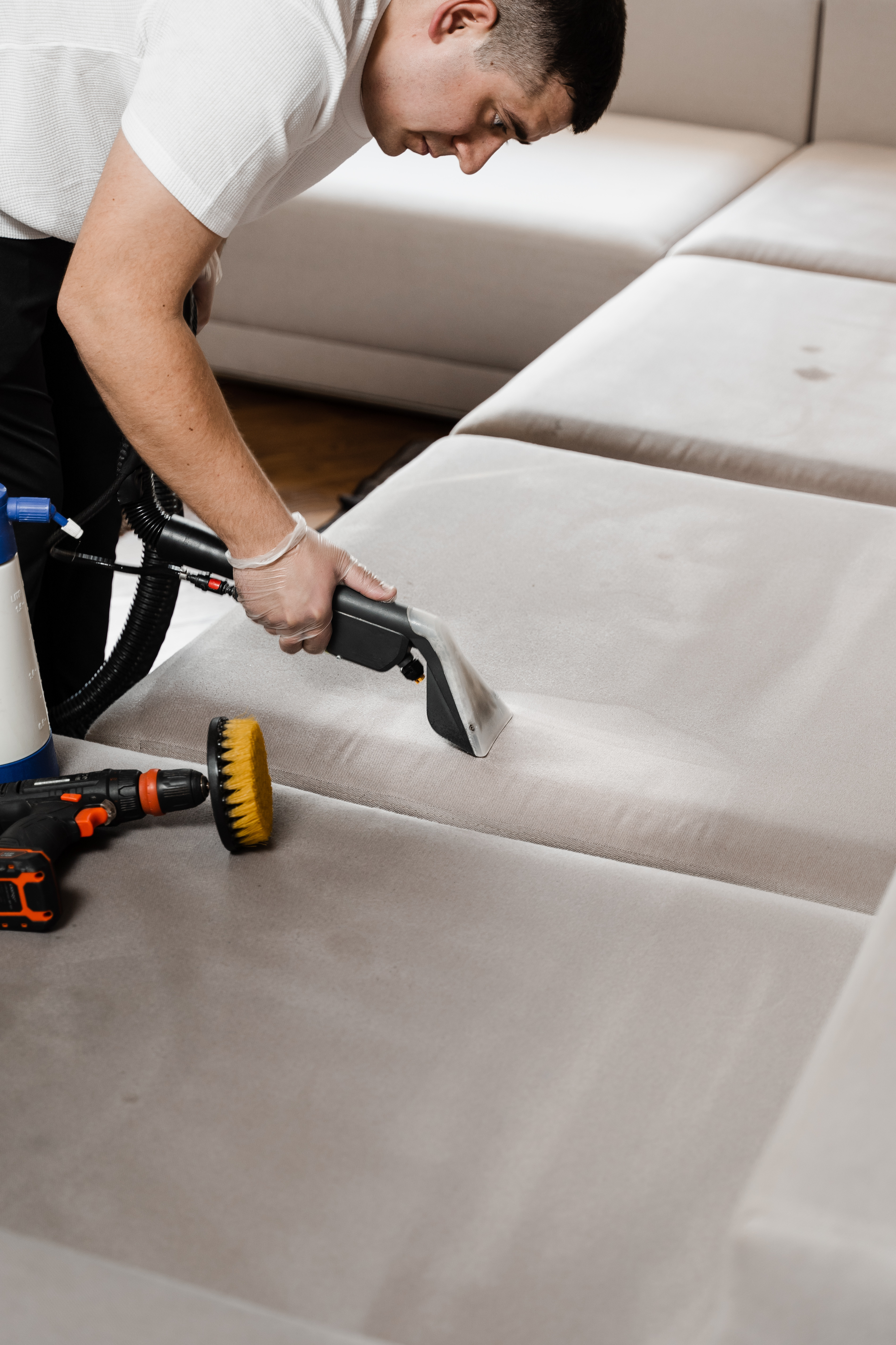 Cleaner is cleaning couch with washing vacuum cleaner extractor machine for dry clean upholstered furniture. Housekeeper is extracting dirt from upholstered sofa using dry cleaning extraction machine.